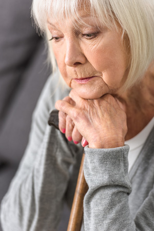 pensive senior woman holding wooden cane and looking downの写真素材