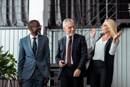 happy businesswoman gesturing while smiling with multicultural partners in officeの写真素材