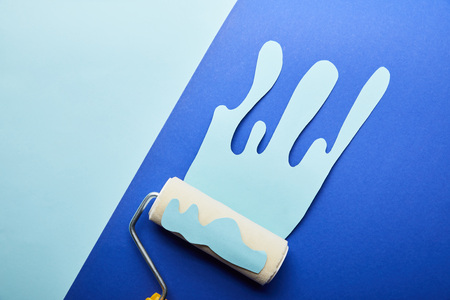 top view of roller with blue paper cut dripping paint on bright blue background