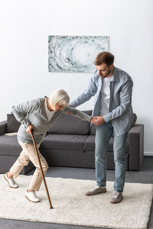 full length view of man helping sick senior mother with caneの写真素材