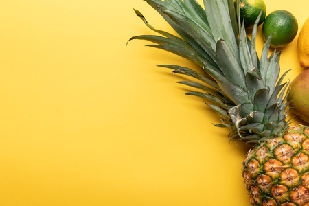 top view of whole ripe pineapple, citrus fruits and mango on yellow backgroundの写真素材