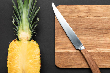 top view of ripe pineapple half on wooden chopping board with knife on black backgroundの写真素材