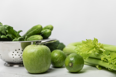 selective focus of sweet apple near green limes and cucumbers on whiteの写真素材