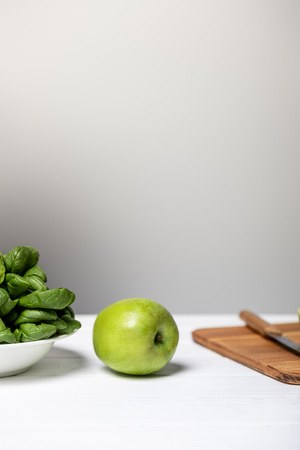 plate with spinach leaves near green apple and cutting board on greyの写真素材