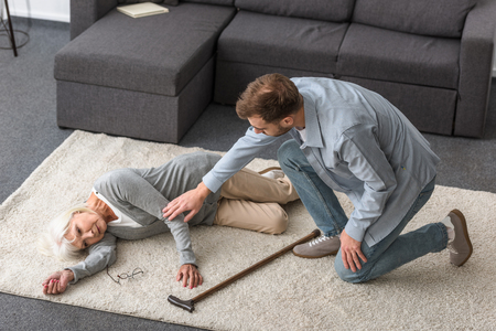 overhead view of adult man with sick senior mother lying on carpetの写真素材