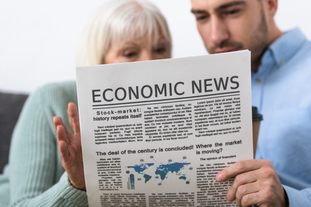 selective focus of man and senior mother reading newspaper at homeの写真素材