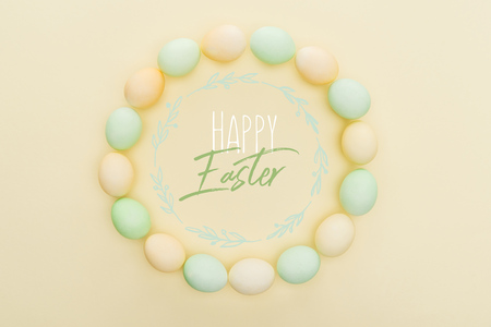 Top view of round frame made of painted chicken eggs on light yellow background with happy Easter...