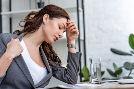Pretty businesswoman with closed eyes suffering from heat in officeの写真素材