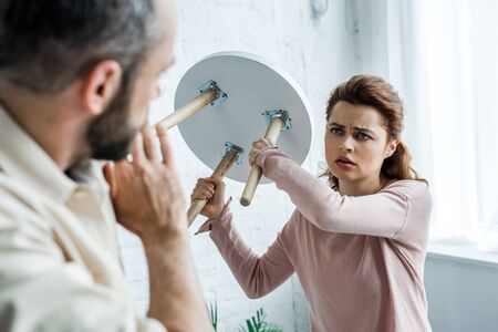 Selective focus of offended woman holding chair and looking at scared man at homeの写真素材