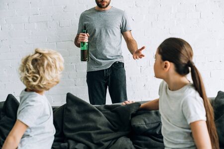 Cropped view of alcohol addicted father with beer and upset children on sofaの写真素材