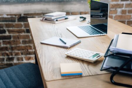 Wooden desk with laptop, pen, notebook and calculator in loft officeの写真素材