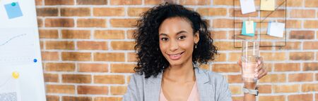 Panoramic shot of African American Casual businesswoman holding glass of water in office