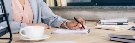 Panoramic shot of African American Casual businesswoman writing in notebook at desk