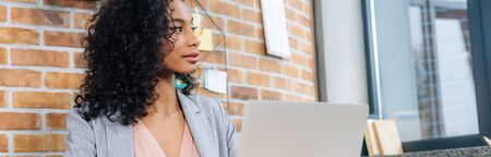 Panoramic shot of beautiful Casual African American businesswoman using laptop in loft office