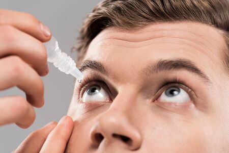 Cropped view of young man applying eye drops isolated on grey background