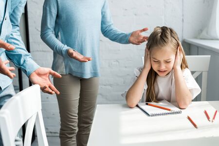 Cropped view of parents near upset kid with closed eyes covering ears