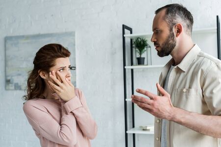 Scared woman touching face and looking at angry man at homeの写真素材