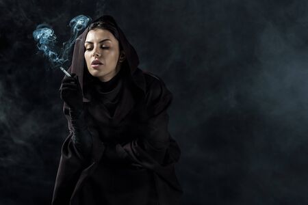 Woman in death costume smoking cigarette on black background