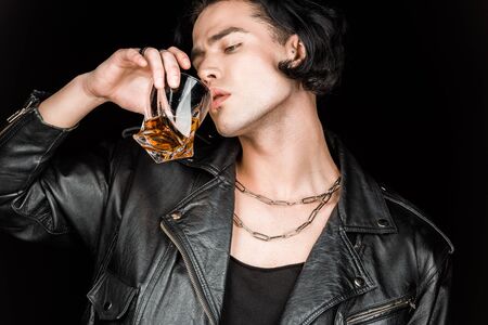Handsome man in leather jacket drinking whiskey isolated on black background