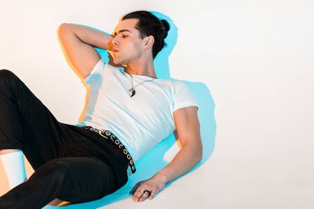 Pensive man in white t-shirt lying on white background with illuminationの写真素材