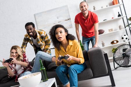 Low angle view of happy multicultural girls playing video game near friends