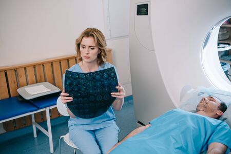 Attentive radiologist examining radiology diagnosis near patient lying on mri scanner bed