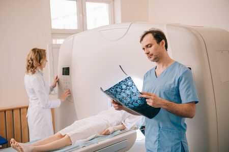 Attentive doctor looking at tomography diagnosis while radiographer operating ct scanner during patients diagnosticsの写真素材