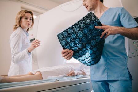 Selective focus of doctor holding tomography diagnosis while radiologist operating ct scanner during patients diagnosticsの写真素材
