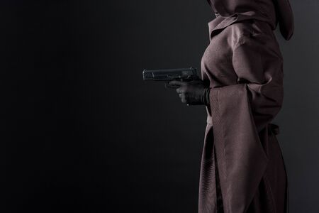 Partial view of woman in death costume holding gun on black background