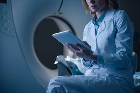 Partial view of radiologist holding digital tablet with x-ray diagnosis while sitting near ct...