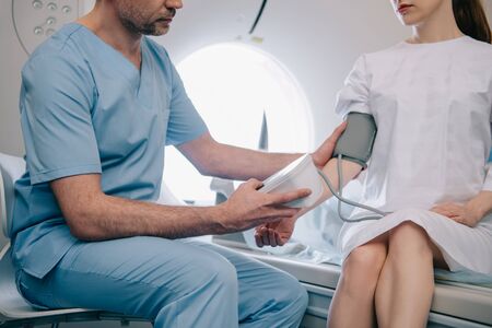Partial view of doctor measuring patients blood pressure with tonometer while sitting at ct scanner