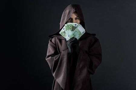 Front view of woman in death costume holding euro banknotes isolated on black backgroundの写真素材