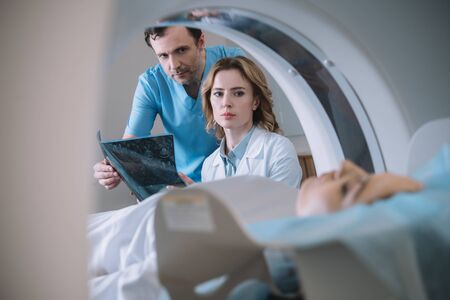 Selective focus of doctors holding x-ray diagnosis and looking at woman during diagnostics on computed tomography scannerの写真素材