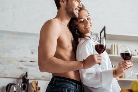Low angle view of happy muscular man holding wine glass near attractive and happy girl at homeの写真素材