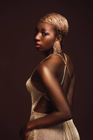 Beautiful fashionable African American girl with short hair isolated on brown backgroundの写真素材
