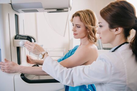 Attentive radiographer adjusting x-ray machine for mammography test while standing near patientの写真素材