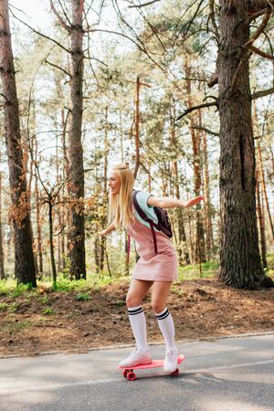 Full length view of blonde girl in knee socks skateboarding on roadの写真素材