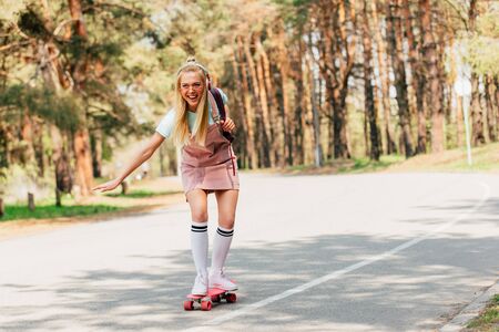 Full length view of excited blonde girl skateboarding and listening music in headphonesの写真素材