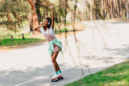 Full length view of African American girl skateboarding and listening music in headphonesの写真素材