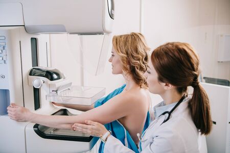 Young radiographer standing near patient while making mammography test on x-ray machineの写真素材