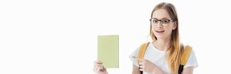 smiling schoolgirl with backpack pointing with finger at book isolated on white, panoramic shot