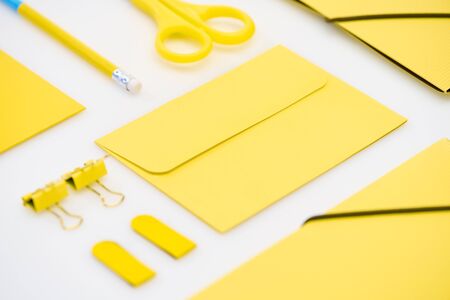 flat lay of yellow envelope, pencil, stickers, scissors and paper clips on white background