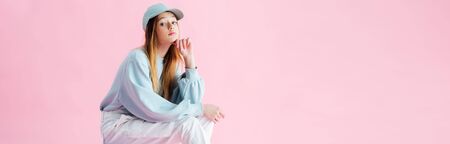 panoramic shot of thoughtful teenage girl in cap isolated on pink