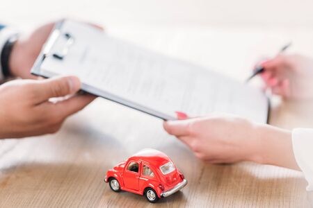 partial view of car dealer giving clipboard to client near miniature carの写真素材
