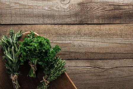 top view of green rosemary, parsley and thyme on chopping board on wooden weathered table with copy spaceの写真素材