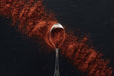 top view of red pepper scattered near silver spoon on textured black backgroundの写真素材