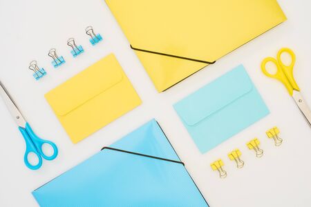 top view of yellow and blue envelopes, folders, paper clips and scissors isolated on white