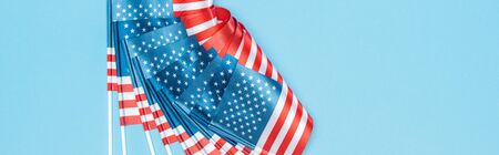 panoramic shot of glossy american flags on sticks on blue background