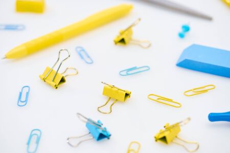 selective focus of yellow and blue paper clips with pen, eraser, scissors and pencil sharpener on...
