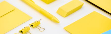 panoramic shot of yellow pen, paper clips, eraser, stickers and envelope on white backgroundの写真素材